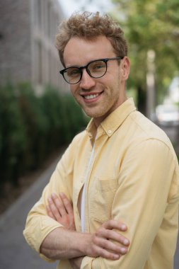 Sarı gömlekli ve şık gözlüklü yakışıklı bir adamın sokakta duran kameraya bakışının portresi. Başarılı iş ve kariyer kavramı