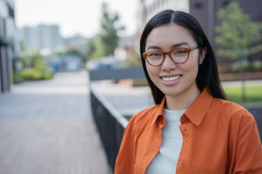 Kendine güvenen başarılı bir iş kadınının özgün portresi. Gözlüklü gülümseyen Asyalı öğrenci üniversite kampüsünde kameraya bakıyor. Eğitim kavramı, kopyalama alanı 