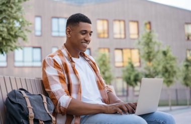 İnternette çalışan, yakışıklı, gülümseyen bir bilgisayar programcısı. Üniversite kampüsünde oturan Afrikalı Amerikalı öğrenci, eğitim konsepti. Metin yazarı yazma, planlama projesi 