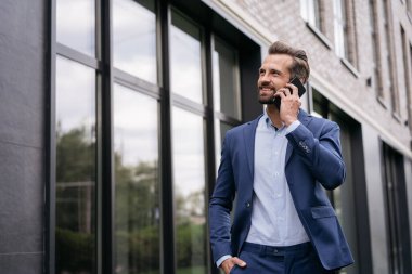 Yakışıklı gülümseyen iş adamı cep telefonuyla konuşuyor.