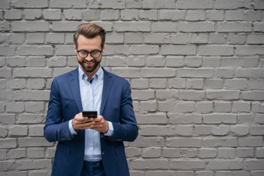 Kendine güvenen, takım elbiseli, şık gözlükler takan cep telefonu kullanan, sokakta durup alışveriş yapan, fotokopi çeken bir adam. Yakışıklı iş adamı iletişimi gri arka planda izole edildi