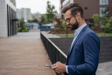 Kendine güvenen iş adamı, iletişim kuran, sokakta duran, kopyalama alanı. Cep telefonu tutan yakışıklı sakallı adam, modern teknoloji kullanarak yemek sipariş ediyor.
