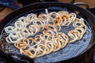 Jalebi hamurunu yağda kızartmak. Kırmızı ve turuncu hamurlu hamur tatmak için şeker şurubuna batırılacak. Jalebi popüler bir atıştırmalıktır..
