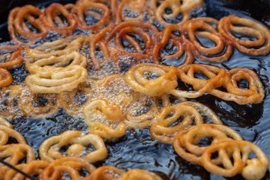 Jalebi hamurunu yağda kızartmak. Kırmızı ve turuncu hamurlu hamur tatmak için şeker şurubuna batırılacak. Jalebi popüler bir atıştırmalıktır..