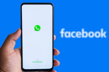 Katmandu, Nepal - 14 Ocak 2021: Arkaplanda WhatApp logosu ile Facebook logosu arasında akıllı telefon bulunduran adam.