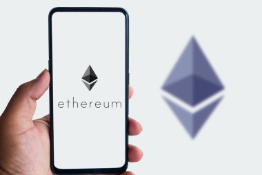 Ethereum logosuna sahip akıllı telefonu tutan adam izole edilmiş arkaplanı tarıyor.