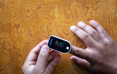 Vücuttaki oksijen doygunluğunu ölçmek için nabız ölçer. Asyalı erkek elleri oksijen seviyesini ölçmek için işaret parmağını taşınabilir oksimetrenin içine koyuyor.