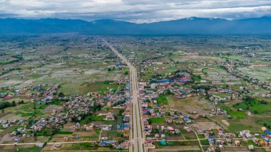 Altı şeritli otobanın havadan görünüşü çayırları, tarlaları ve dağları geçerek Nepal kırsalındaki dağlara doğru yayılmış evleri gösteriyor..