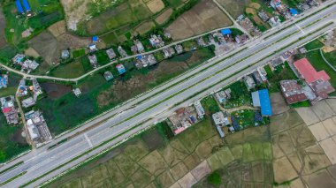Altı şeritli otobanın havadan görünüşü çayırları, tarlaları ve dağları geçerek Nepal kırsalındaki dağlara doğru yayılmış evleri gösteriyor..