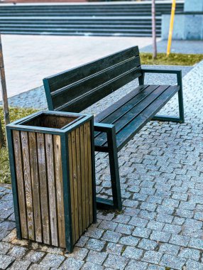 Çağdaş ahşap ve metal bankta kaldırım taşında çöp tenekesi var.