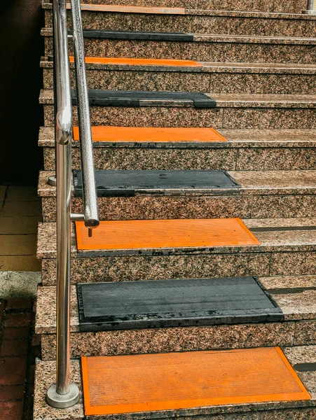 vertical view of granite stairs with orange and black anti-slip mats and metal railing