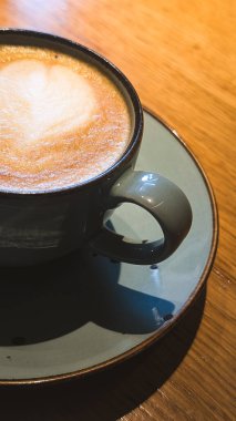 Yumuşak gölgeli ahşap bir masada bir fincan kapuçinonun dikey yakın çekimi