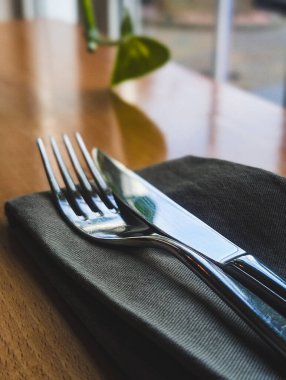 Gümüş bir bıçak ve çatalın dikey yakın çekimi. Ahşap bir restoran masasındaki koyu gri bir peçeteye düzgünce yerleştirilmiş.