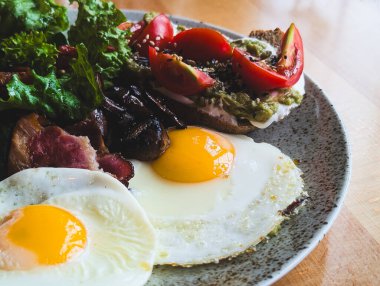 Yağda yumurta, pastırma, taze marul ve domatesli avokado tostu.