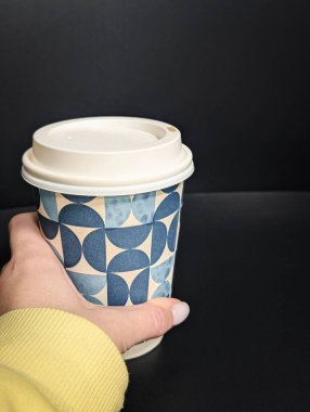 Siyah minimalist arka plana karşı geometrik bir kahve fincanı tutarken dikey yakın plan