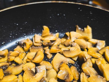 Dilimlenmiş kahverengi mantarları kapayın (şampiyonlar) siyah yapışmaz tavada kızartıyorlar.