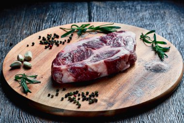 Domuz yağı katmanlı çiğ domuz eti pişirmeye hazır, ahşap bir tahtanın üzerinde sarımsak, biberiye, tuz ve biber ile birlikte yatıyor..