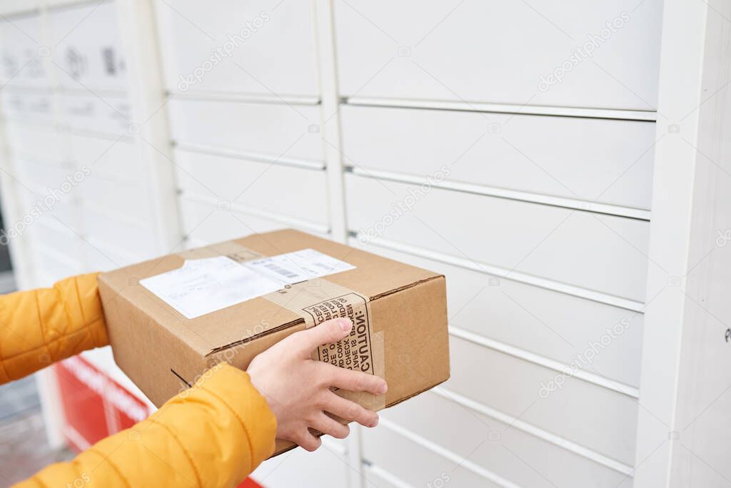 the girl stands near the post office and sends the package to the parcel locker. Receiving package. brown cardboard packaging