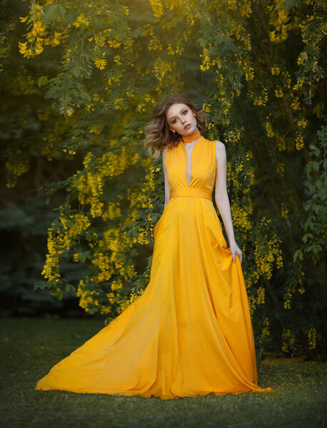 Woman in fluttering yellow long dress under a blossoming tree with yellow flowers, waving silk cloth, artistic processing.
