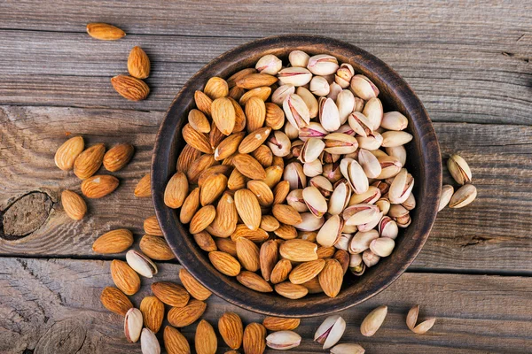 Amandelen en pimpernoten (pistaches) op een houten kom, rustieke achtergrond — Stockfoto