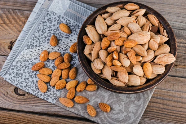 Amandelen en pimpernoten (pistaches) op een houten kom, rustieke achtergrond — Stockfoto