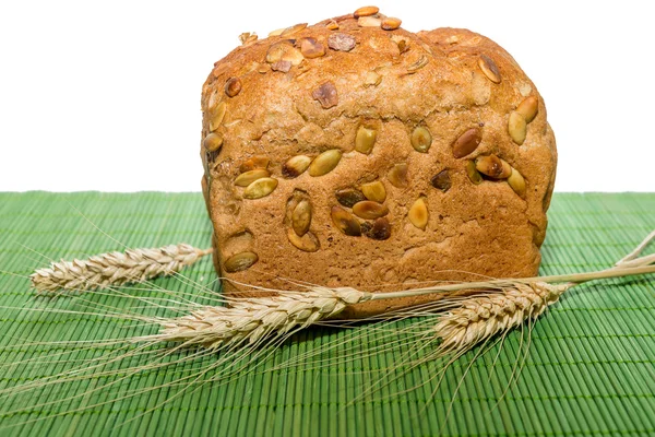 Whole grain bread with ears of wheat on green mat — Stock Photo, Image