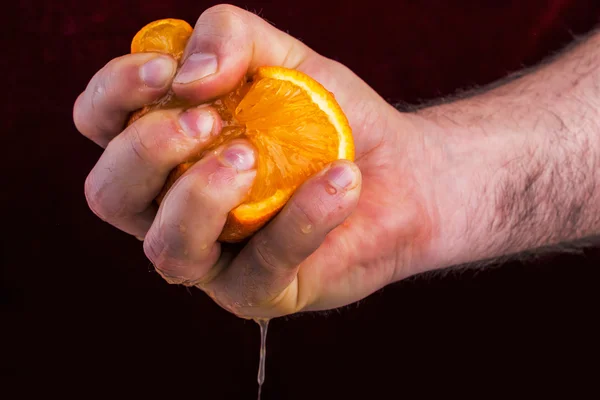 Male hand squeezing orange on mulberry background. — Stock Photo, Image