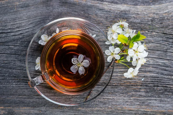 Taza de té y rama de cereza sobre un fondo de madera . — Foto de Stock