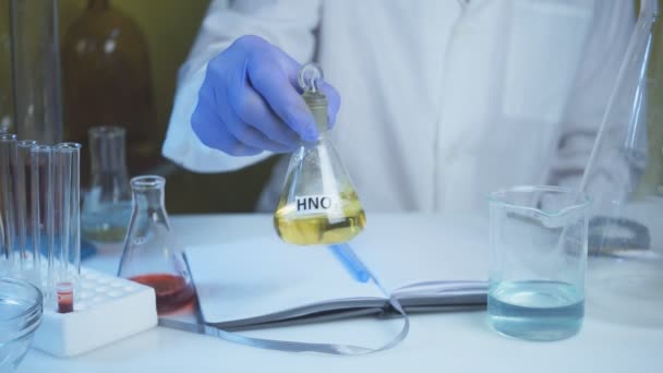 Suministro de alimentos de laboratorio químico. OMG Productos modificados genéticamente en el laboratorio. Un técnico de laboratorio con una bata blanca sostiene ácido nítrico en su mano. — Vídeo de stock