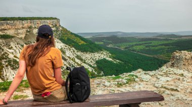 Fotoğraf. Bir kız turist Kırım dağlarının tepesindeki ahşap bir bankta oturuyor. Çok güzel bir manzara sunuyor..