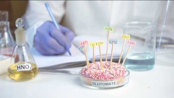 Laboratorio di sicurezza alimentare, concetto di scienziato. Ispettore che fa ricerche in laboratorio. La ciambella sul tavolo è decorata con tavolette con i nomi degli additivi di E. — Video Stock