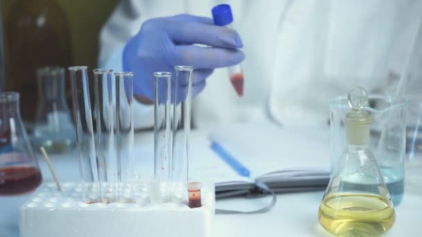 Scientist tests blood and adds test tube in rack at lab. Concept of health and safety life. — Stock Video