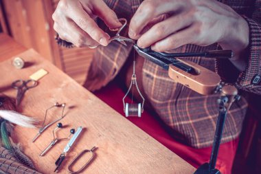 Fotoğraf. Balık tutmak için sinek bağlayan genç adamın ellerini kapat.