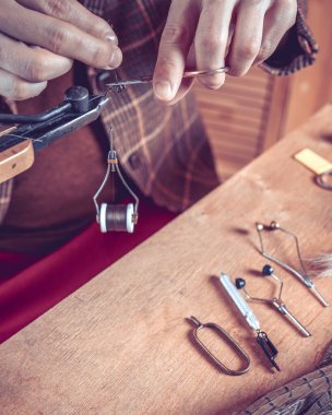 Fotoğraf. Balık tutmak için sinek bağlayan genç adamın ellerini kapat.