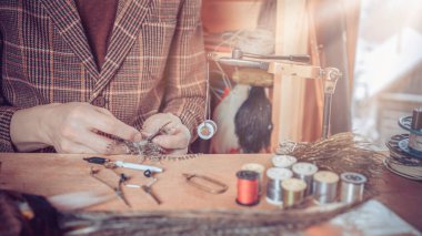 Fotoğraf. Balık tutmak için sinek bağlayan genç adamın ellerini kapat.
