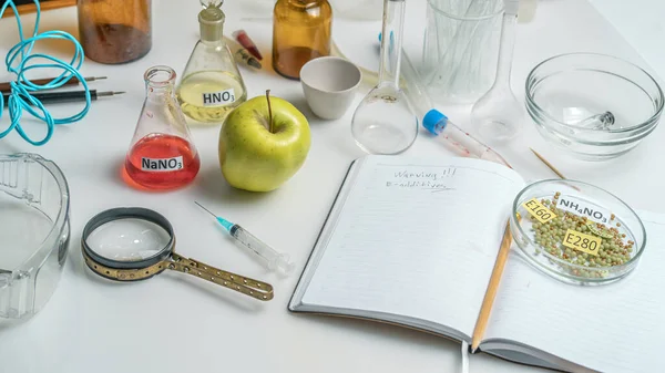 Food safety laboratory. View of a fresh ripe apple with test tubes and tools on a table with an open notepad in a research laboratory. The concept of genetic modification of fruits.