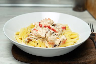 Tahtanın üzerinde duran beyaz tabakta deniz mahsullü makarna.