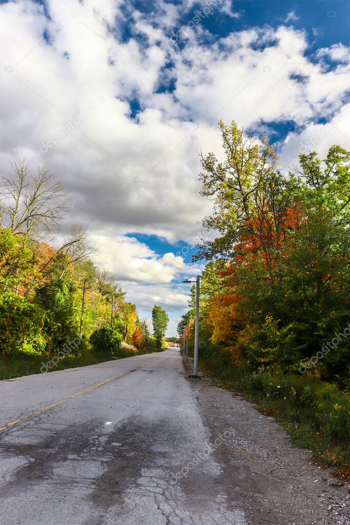 Cloud filled sky above a lonely road with beautiful fall foliage, ON, Canada