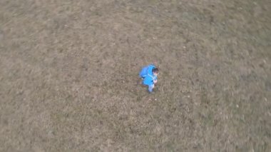 Mavi ceketli ve mavi sırt çantalı bir erkek otlakçı çayırda yürür ve drone tarafından filme alınır.