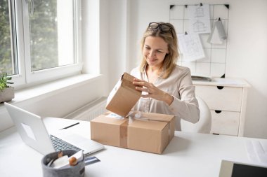 Sarışın iş kadını ofisinde oturuyor ve internetten bazı paketler, hediyeler alıyor ve mutlu.