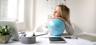 Bayan mimar ofisinde oturuyor ve elinde bir küre tutuyor ve dünyayı dolaşmayı hayal ediyor.