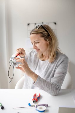 Ofisteki masada oturan sarışın kadın elektrikçi prizi tamir ediyor.