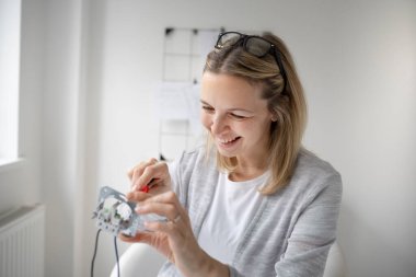 Ofisteki masada oturan sarışın kadın elektrikçi prizi tamir ediyor.