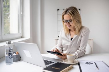 Ofiste dizüstü bilgisayarda çalışan gözlüklü bir iş kadını.