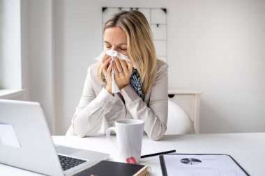 Ofisteki hasta iş kadını laptopunun önünde oturup burnunu silmekten rahatsız oluyor. Stresli kadın işyerinde panik atak geçiriyor.