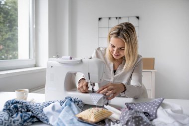 Kafkasyalı moda tasarımcısı stüdyosunda dikiş makinesiyle oturup güzel elbiseler dikiyor.