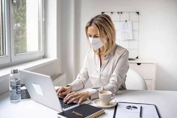 Concept: Corona office challenge, business woman wearing ffp2 mask working on laptop in office