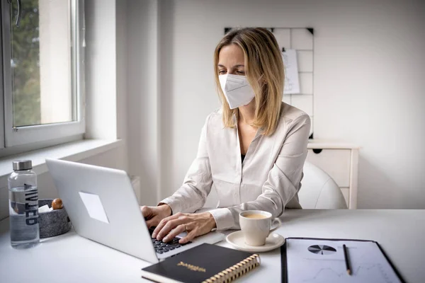 Concept: Corona office challenge, businesswoman wearing ffp2 mask working on laptop in office