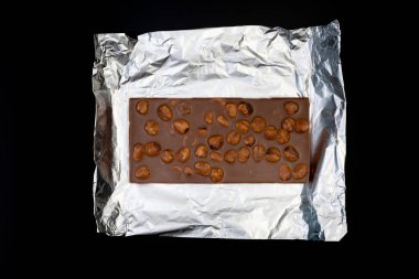 Tatlı ve lezzetli çikolata, gümüş folyoda fındıklar ve siyah arka planda fotoğraf.