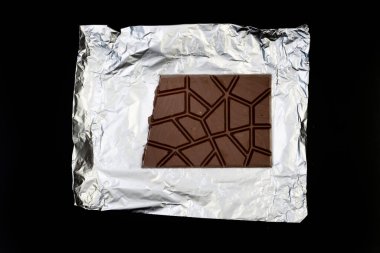 Gümüş folyo üzerine tatlı ve lezzetli çikolata. Yukarıdan çekilmiş siyah arka plan fotoğrafı.